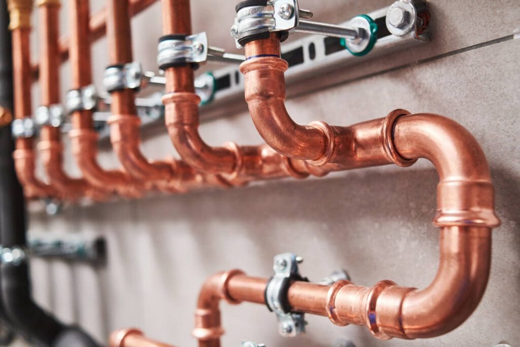 Close-up of multiple copper pipes and fittings mounted on a wall, secured with metal brackets, forming a network typical of a plumbing or heating system installation.
